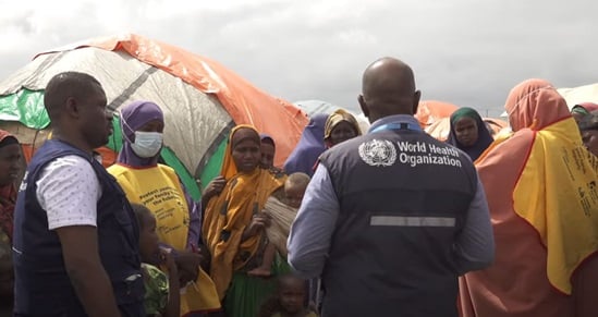 Two staff members of WHO talking to a group of women in a refugee camp